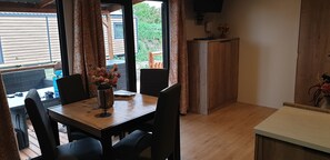 A dining area with a wooden table, black chairs, and a vase of flowers. There is a wooden cabinet and a television mounted on the wall.