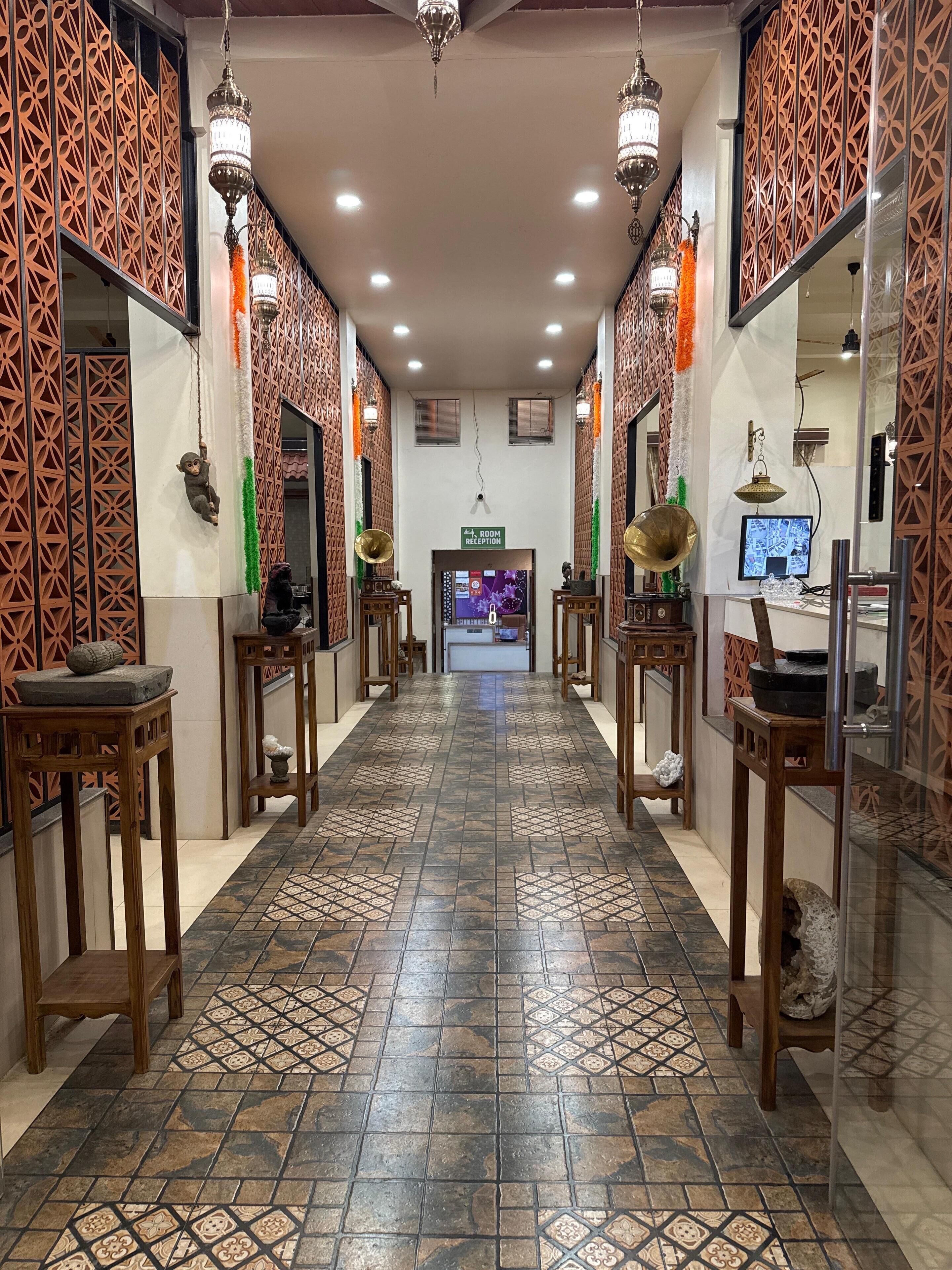 A hotel lobby with patterned tiles, wooden furniture, and decorative elements like hanging lamps and a reception desk.