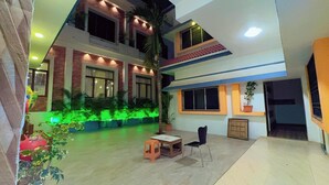 A multi-level building with a courtyard featuring green lighting, potted plants, and outdoor seating.
