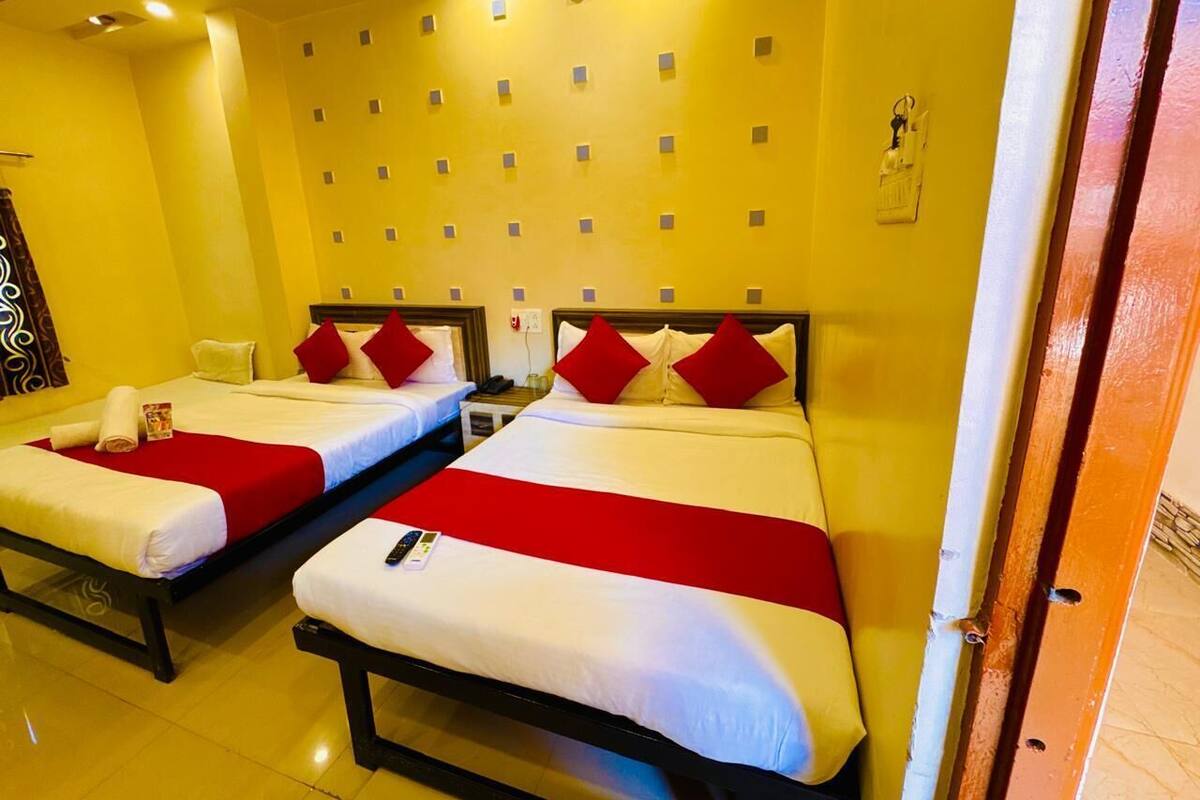 Habitación de hotel con dos camas, cada una con ropa de cama blanca y detalles rojos, y una pared amarilla con diseño estampado.