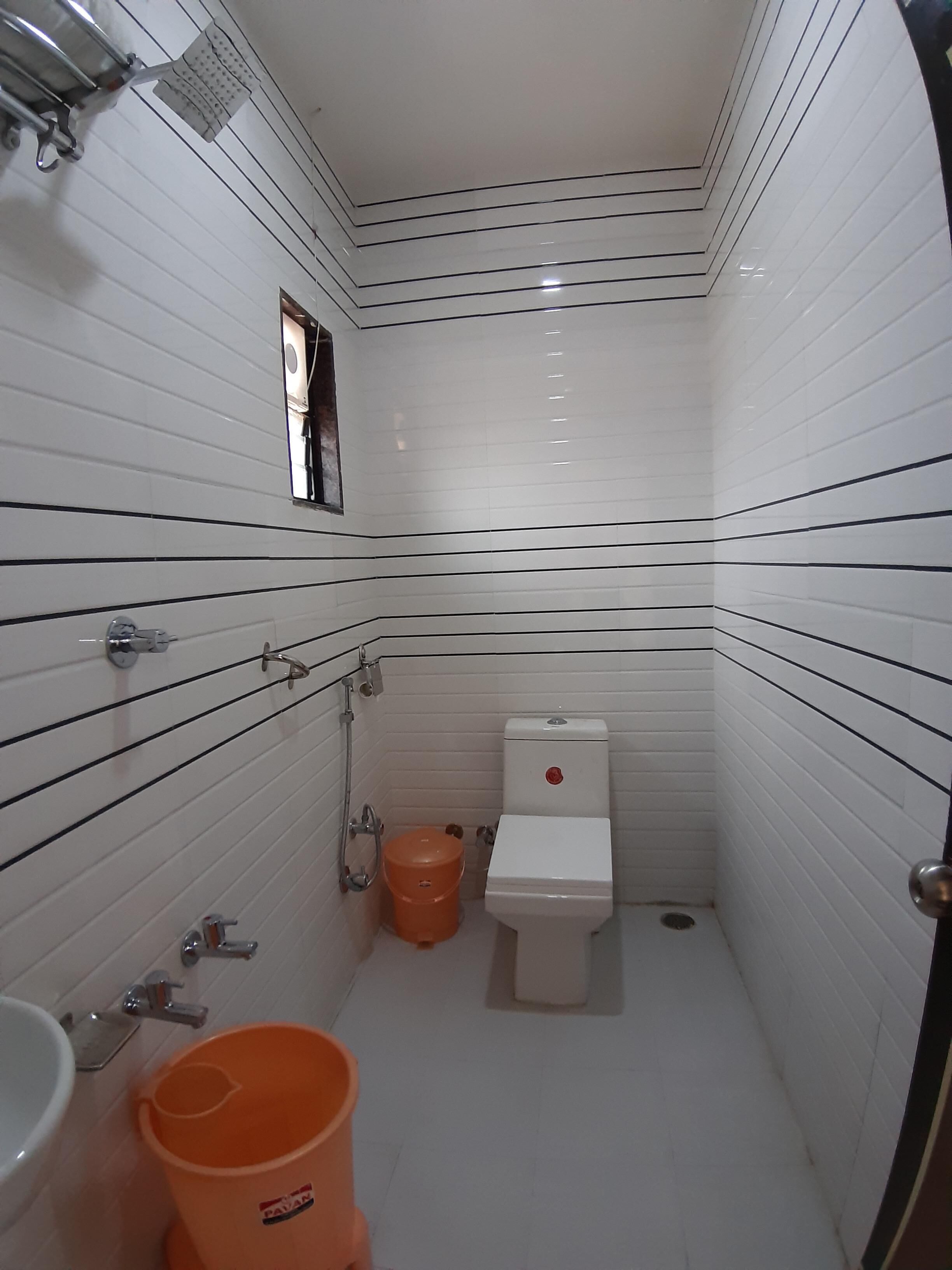 Ein kleines, schmales Badezimmer mit weiß gefliesten Wänden und schwarzen, horizontalen Linien. Es beinhaltet eine Toilette, ein Waschbecken und einen Duschbereich.