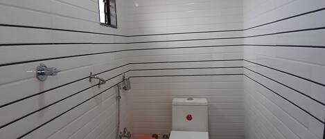 Ein kleines, schmales Badezimmer mit weiß gefliesten Wänden und schwarzen, horizontalen Linien. Es beinhaltet eine Toilette, ein Waschbecken und einen Duschbereich.