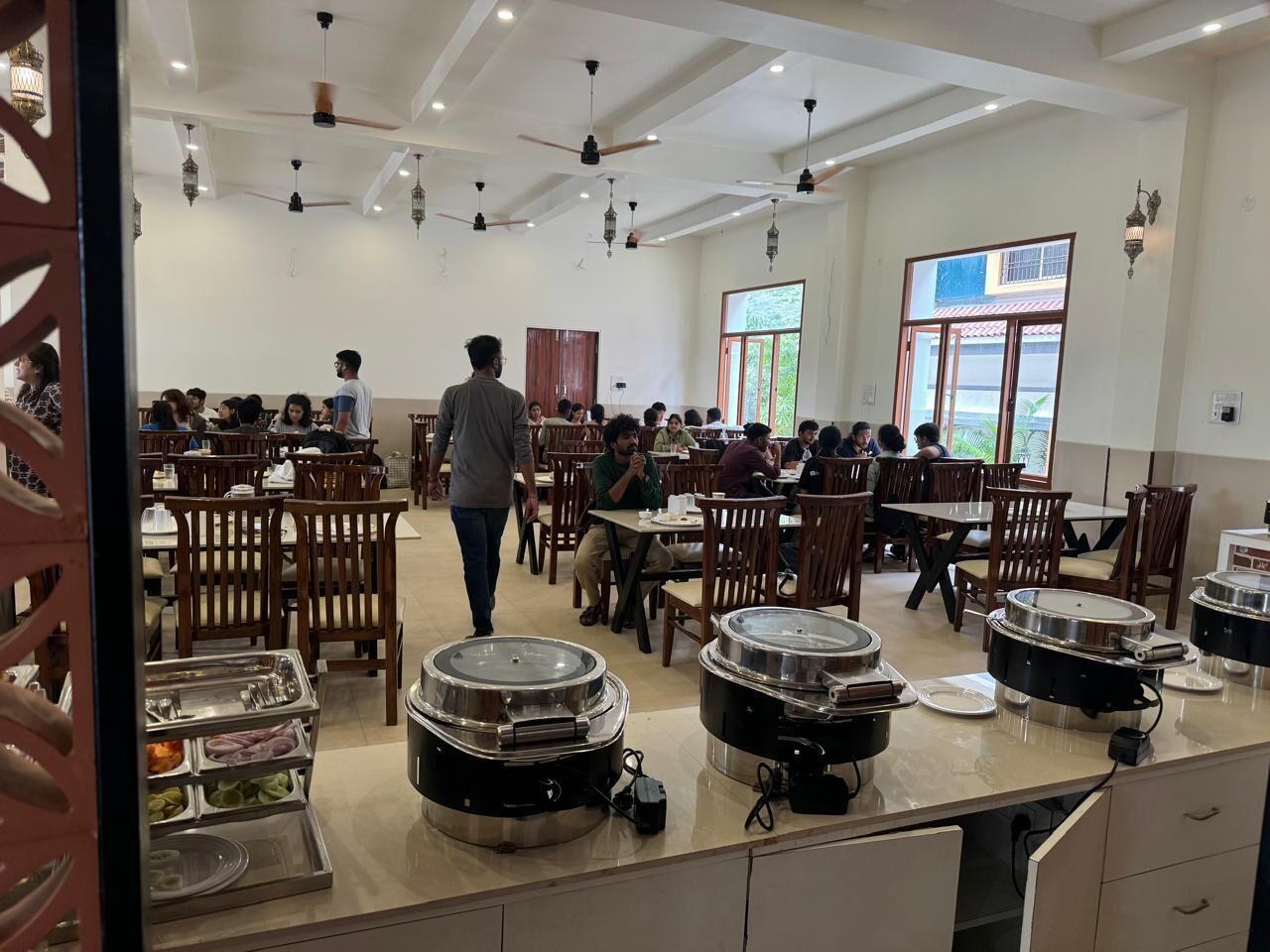 A cafeteria with multiple tables and chairs, buffet stations, and ceiling fans.