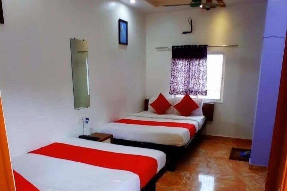 Habitación de hotel con tres camas, ventilador de techo, ventana con cortinas y piso de baldosas.