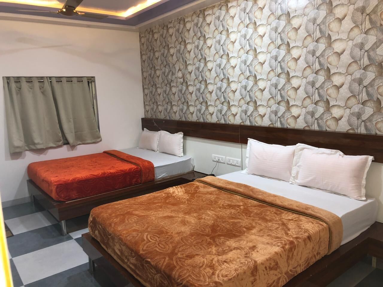 A hotel room with two beds, a patterned wall, and a ceiling fan.