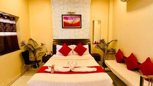 A hotel room with a large bed, a ceiling fan, an air conditioning unit, a painting on the wall, and a red and white color scheme.
