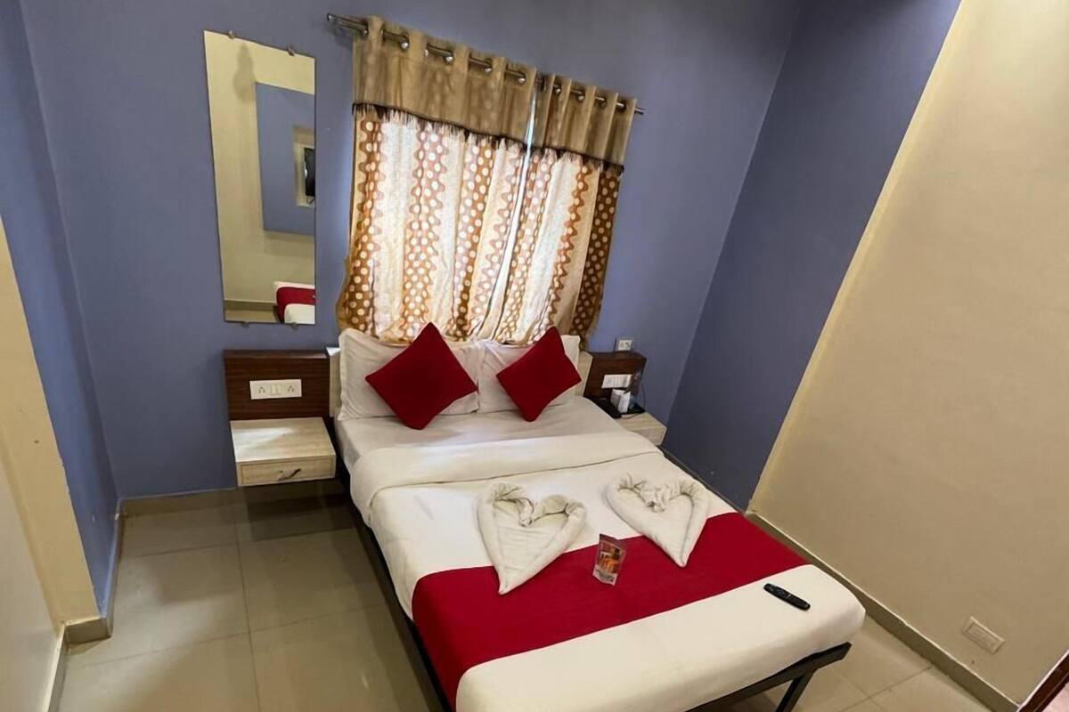 Habitación de hotel con una cama individual, una mesita de noche, un espejo y una ventana con cortinas.