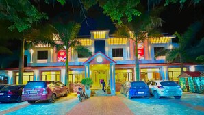 A hotel with a central entrance, multiple cars parked in front, and a paved walkway leading to the entrance.