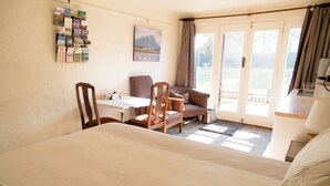A hotel room with a bed, a desk, two chairs, a bookshelf with books, a painting on the wall, and a view through the glass door. - Cosy north facing priv selfcontained Suite set within large garden, 7min to town (Hamilton)