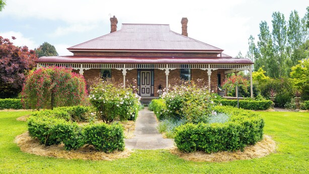 A brick house with a red roof, surrounded by well-maintained gardens and a pathway leading to the entrance. - Cosy north facing priv selfcontained Suite set within large garden, 7min to town (Hamilton)