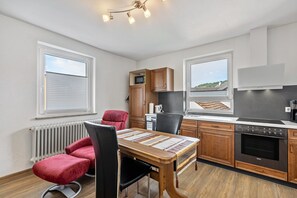 A modern kitchen with wooden cabinets, a built-in oven, and a dining area with a table and chairs.