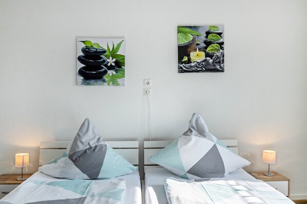 A hotel room with two beds, each with a pillow, a bedside table with a lamp, and two wall-mounted artworks.