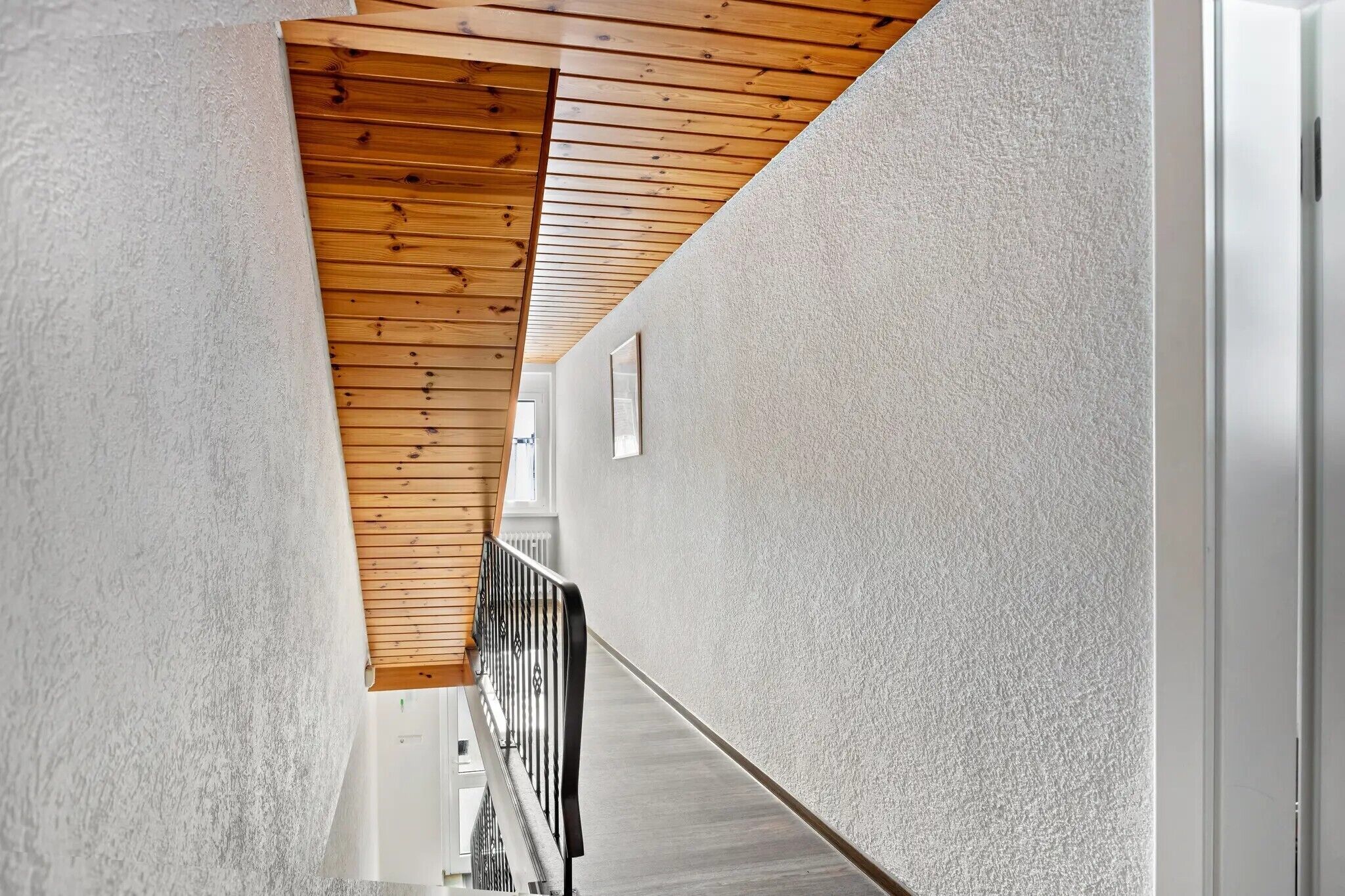 Un couloir doté d’un plafond en lambris de bois et d’un mur blanc à texture.