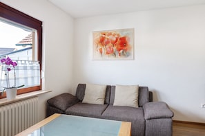 Een woonkamer met een bank, een glazen salontafel, een potplant en een schilderij aan de muur.