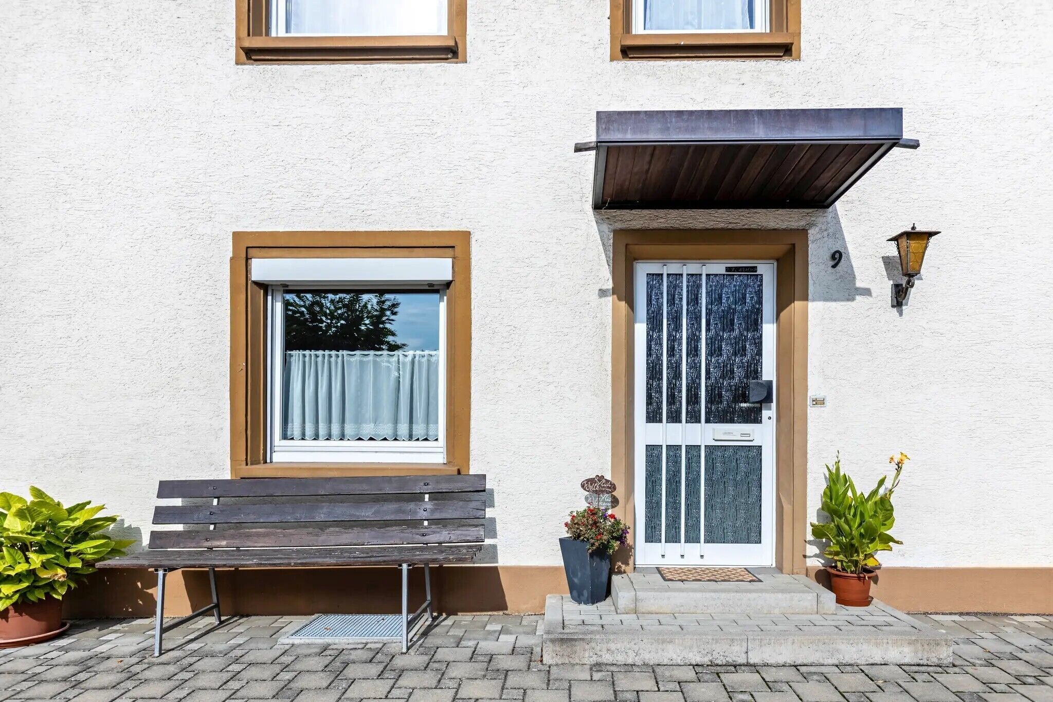 Un bâtiment avec un banc à l’extérieur, une porte dotée d’un panneau de verre et deux plantes en pot.