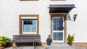 Un bâtiment avec un banc à l’extérieur, une porte dotée d’un panneau de verre et deux plantes en pot.