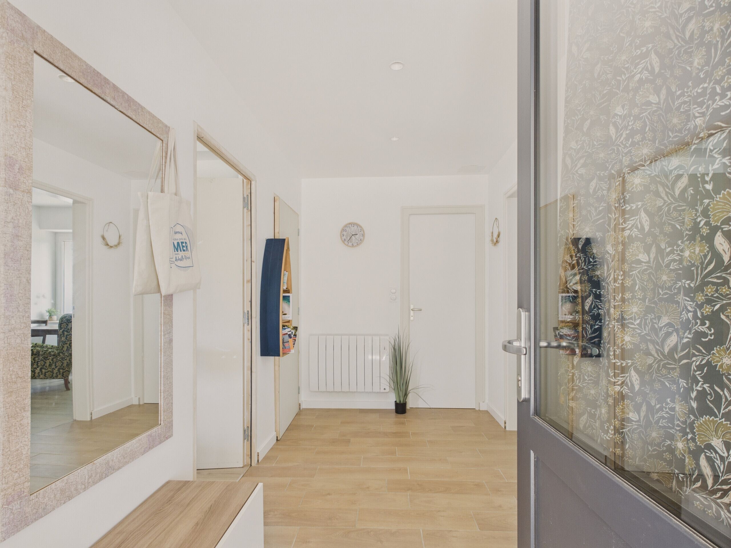 A hallway with a wooden floor, a mirror, a clock, and a door with a floral pattern.