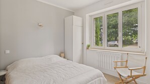 Ein Schlafzimmer mit einem großen Bett, einem Fenster mit Außenblick, einem Heizkörper und einem Holzstuhl.