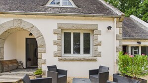 Ein Gebäude mit einem steinernen Bogen, einem Fenster mit weißem Rahmen und Gartenmöbeln aus Rattangeflecht.