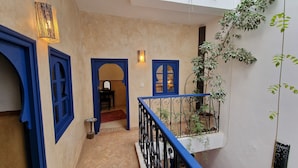 Un couloir étroit, avec des portes à cadre bleu et une petite table surmontée d’un miroir.