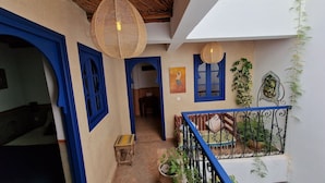 Un couloir étroit avec des portes et des fenêtres bleues, un banc en bois et un escalier doté d’une rampe bleue.