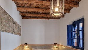 Une chambre avec un plafond en pente, un grand lit recouvert d’une couverture bleue, deux lampes fixées au mur et une fenêtre dotée d’un cadre bleu.