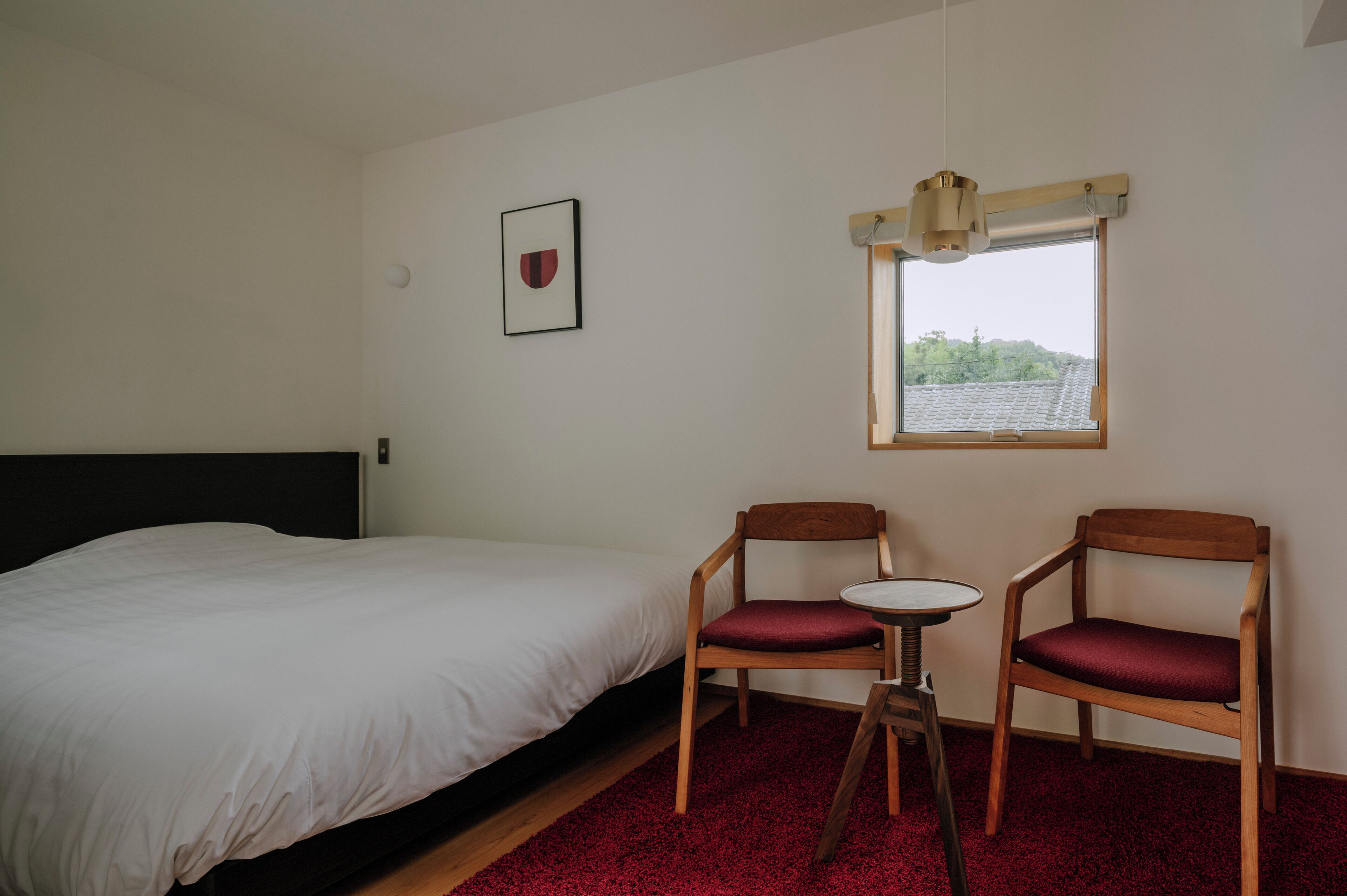 A bedroom with a bed, two wooden chairs, a small table, and a window with a view of buildings.