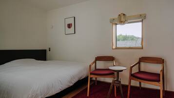 A bedroom with a bed, two wooden chairs, a small table, and a window with a view of buildings.