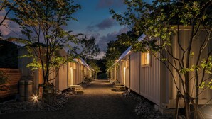 A row of single-story cabins with a gravel path leading to a central point, surrounded by trees. - NANUKA HOTEL (Kirishima)
