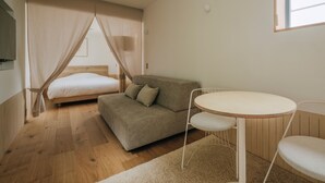 A bedroom with a bed, a sofa, a round table, and a window. - NANUKA HOTEL (Kirishima)