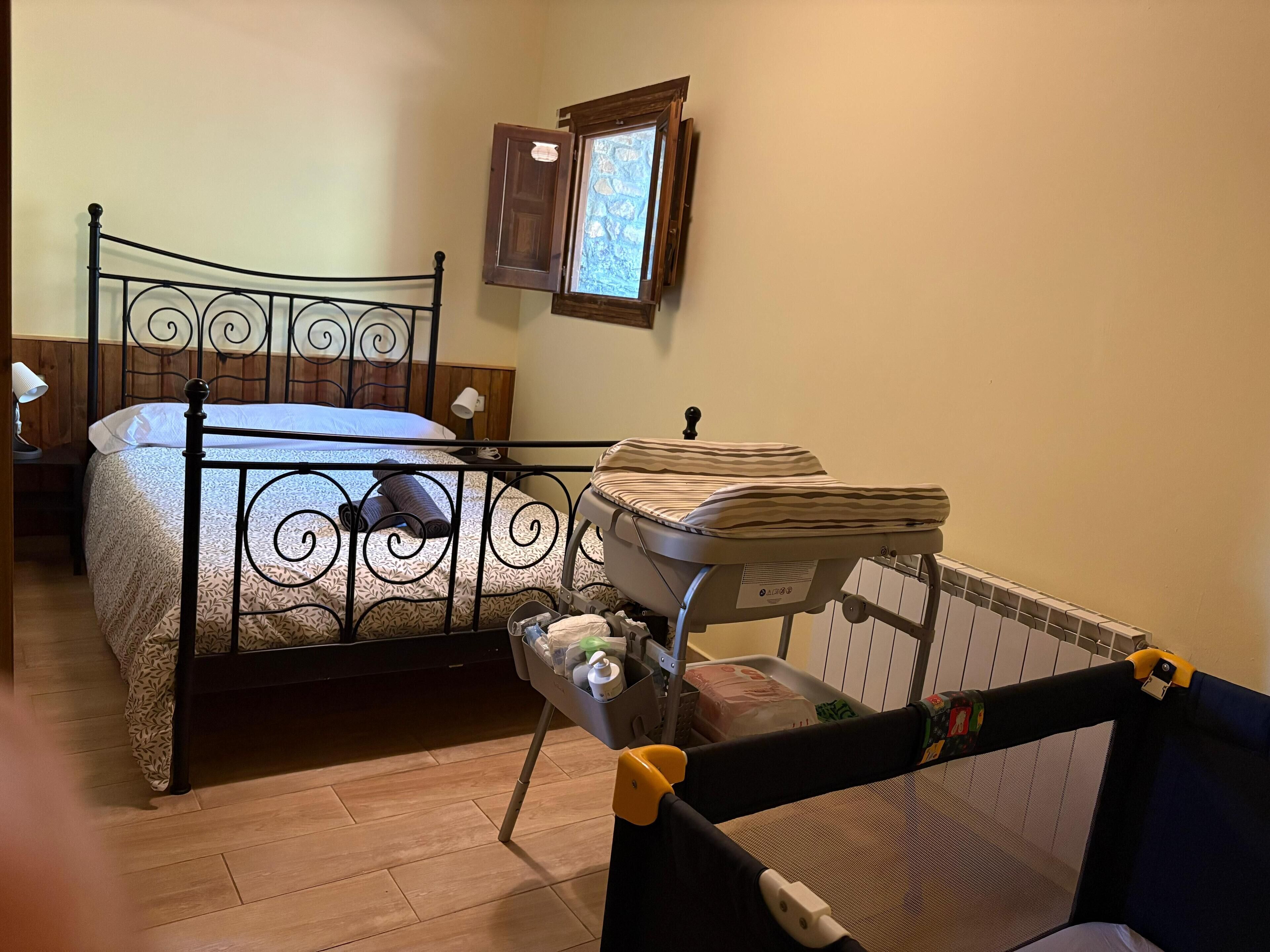 Une chambre à coucher avec un lit, un berceau, une fenêtre et une table de chevet.