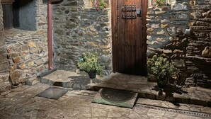 A stone building with a wooden door, potted plants, and a stone wall with a window. - Beautiful and cozy rural house in El Bierzo (Ocero)