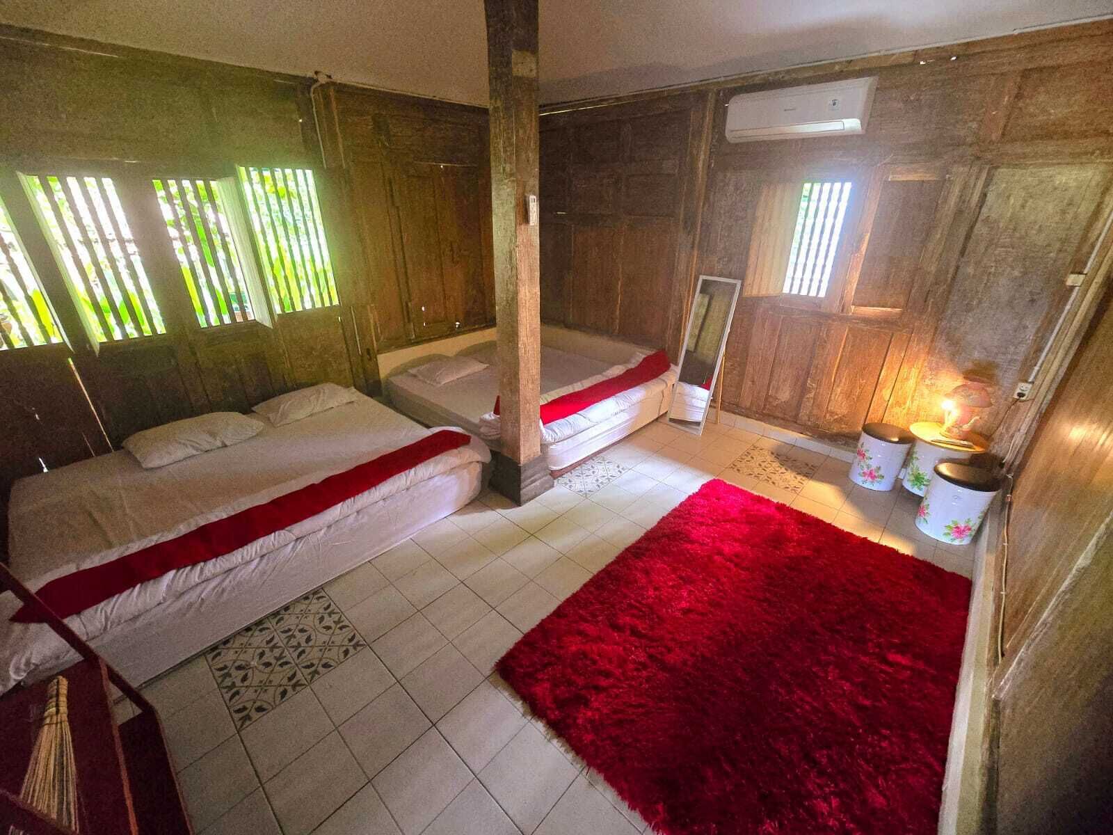 Ein Zimmer mit zwei Betten, einem roten Teppich, Holzwänden und einem Fenster mit Jalousien.