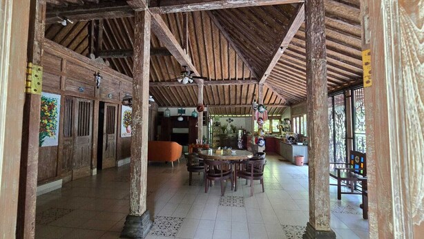A spacious hall with wooden beams and columns, a tiled floor, and a dining area with chairs and a table. - Eyang Residence Limasan Kebon Dalem (Prambanan)