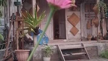 Un edificio rústico con techo de tejas, un porche de madera y diversas macetas con plantas.