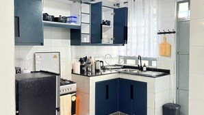Een compacte keuken met witte en blauwe kastjes, een zwarte koelkast, een kookplaat en een gootsteen.
