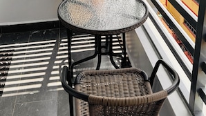 Een balkon met een ronde tafel en twee rieten stoelen, met uitzicht op een stadsgezicht met kleurrijke gebouwen.