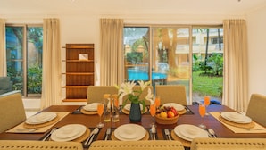 A dining table set with plates, cutlery, and glasses, with a vase of flowers and a fruit basket.