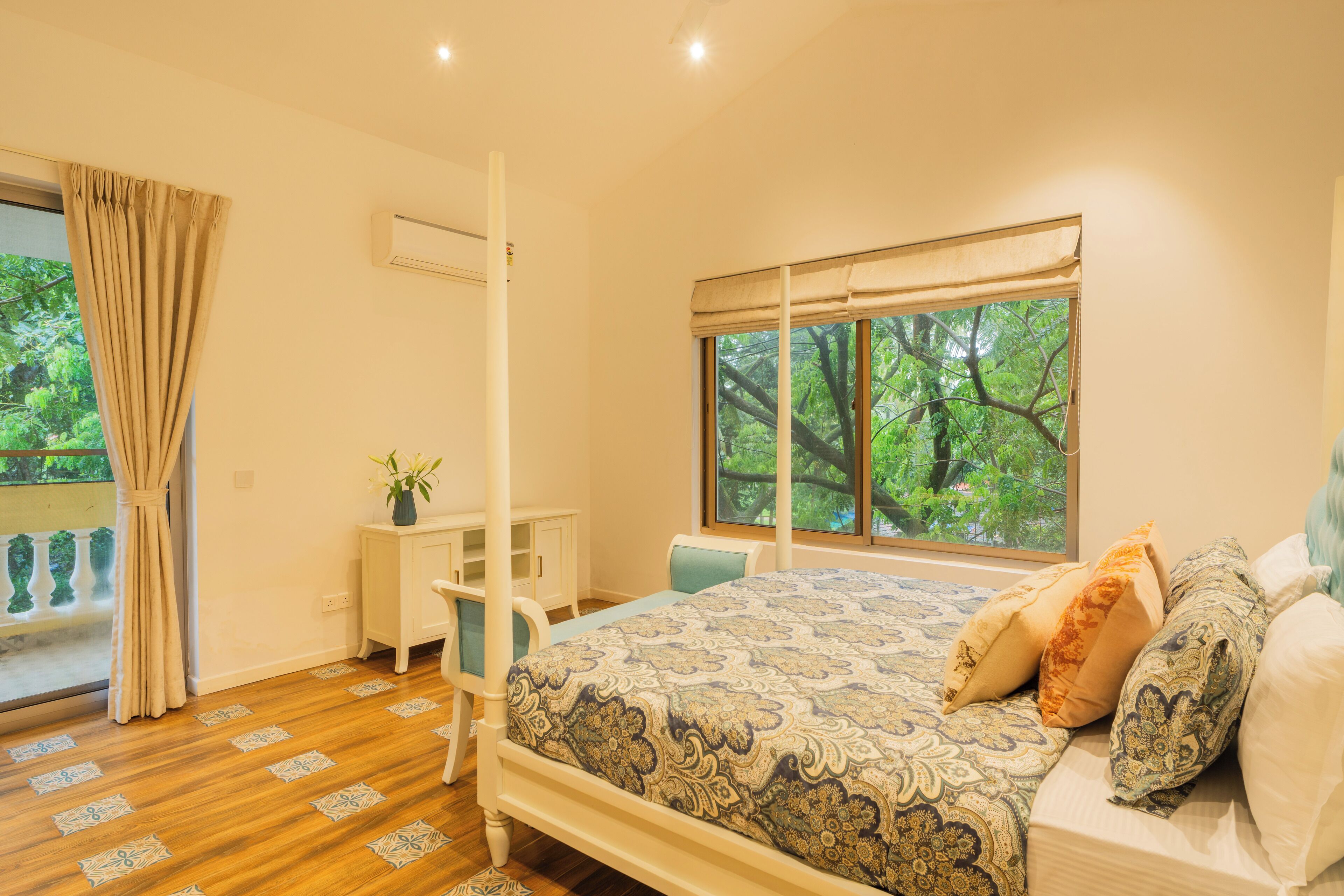 A bedroom with a bed, a desk, a chair, a window with a view of trees, and a curtain.