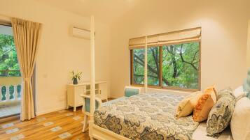 A bedroom with a bed, a desk, a chair, a window with a view of trees, and a curtain.