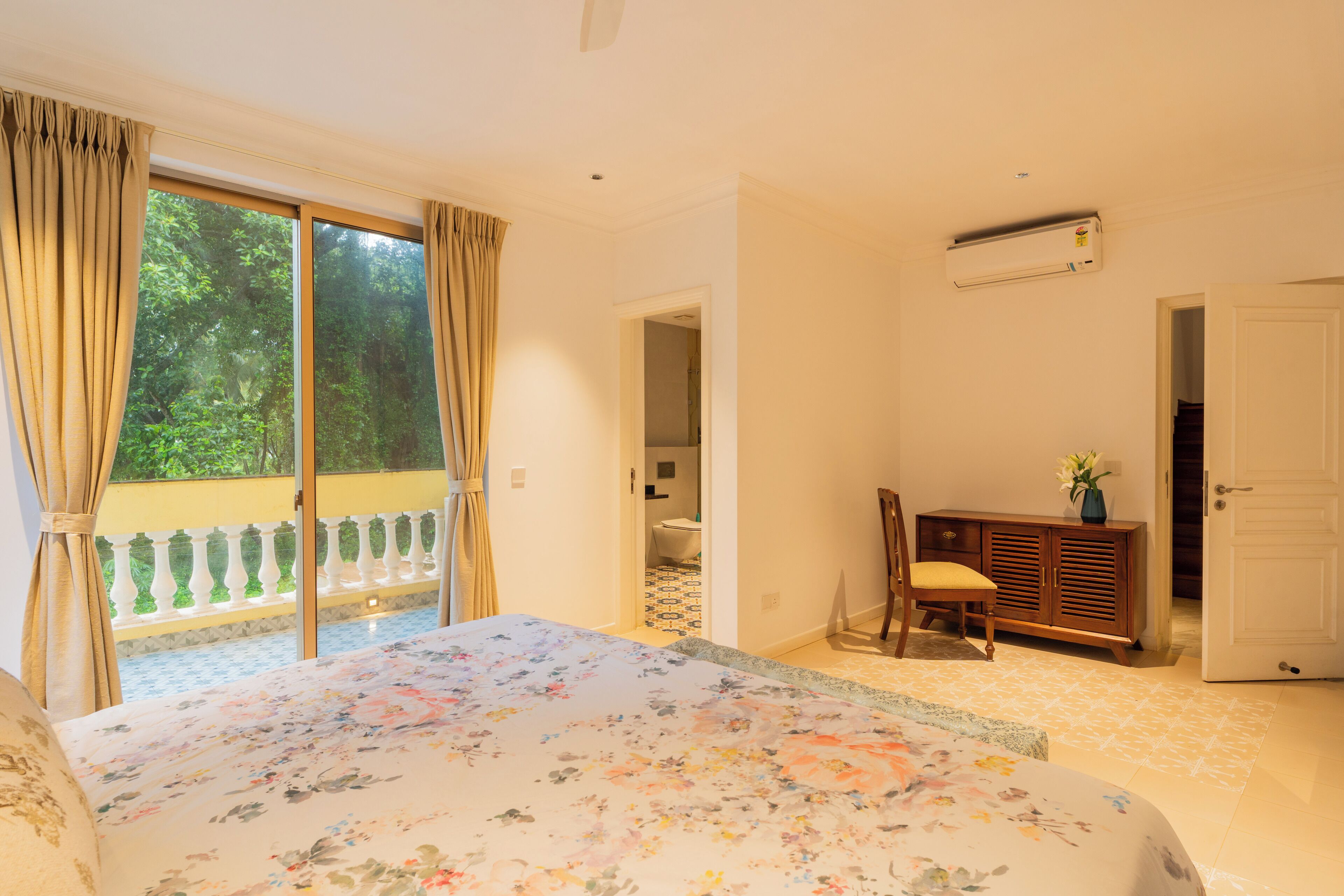 Un dormitorio con una cama grande, un aparador de madera, una silla y un baño visible a través de una puerta abierta.