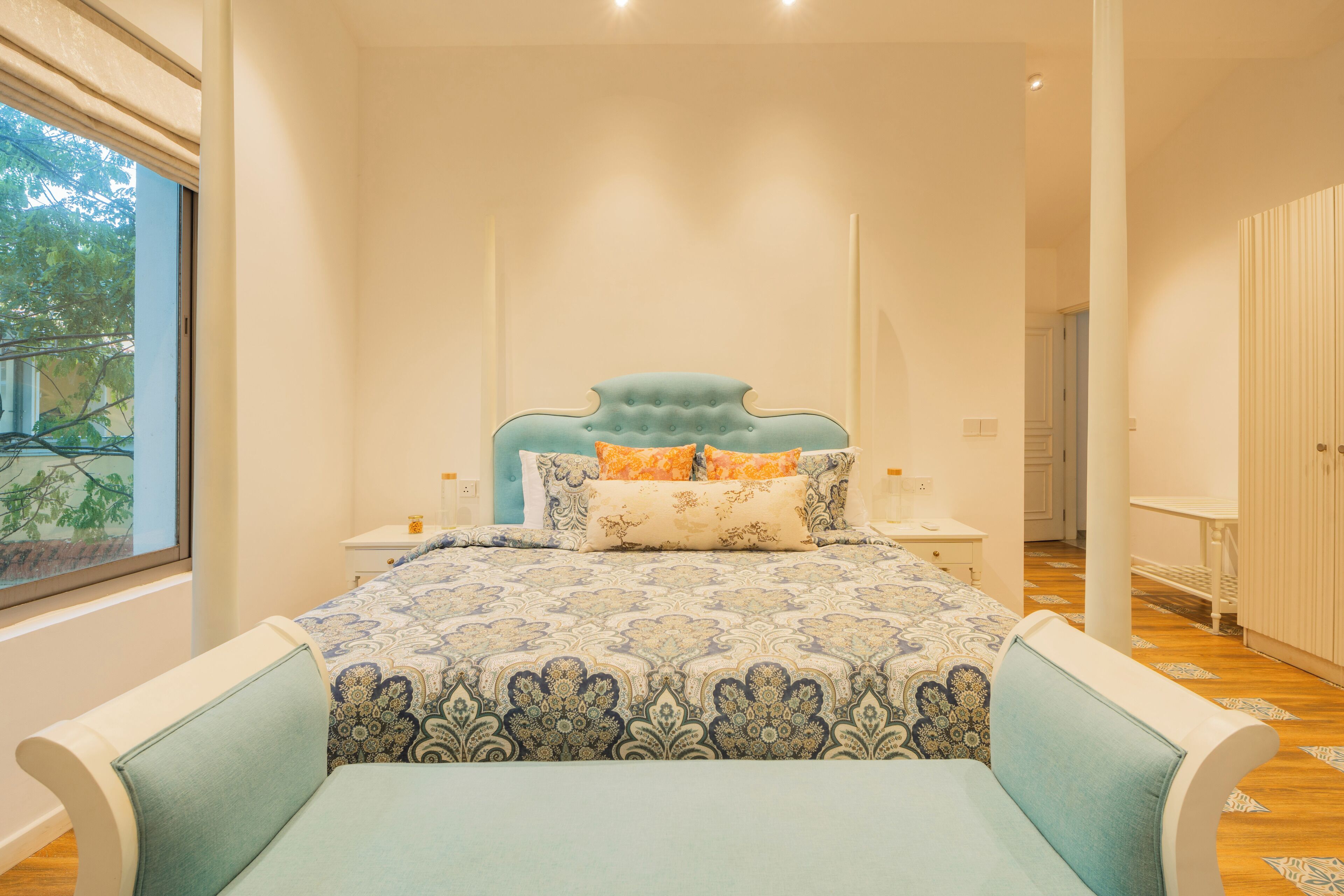 A bedroom with a large bed, two bedside tables, a window, and a view of greenery outside.