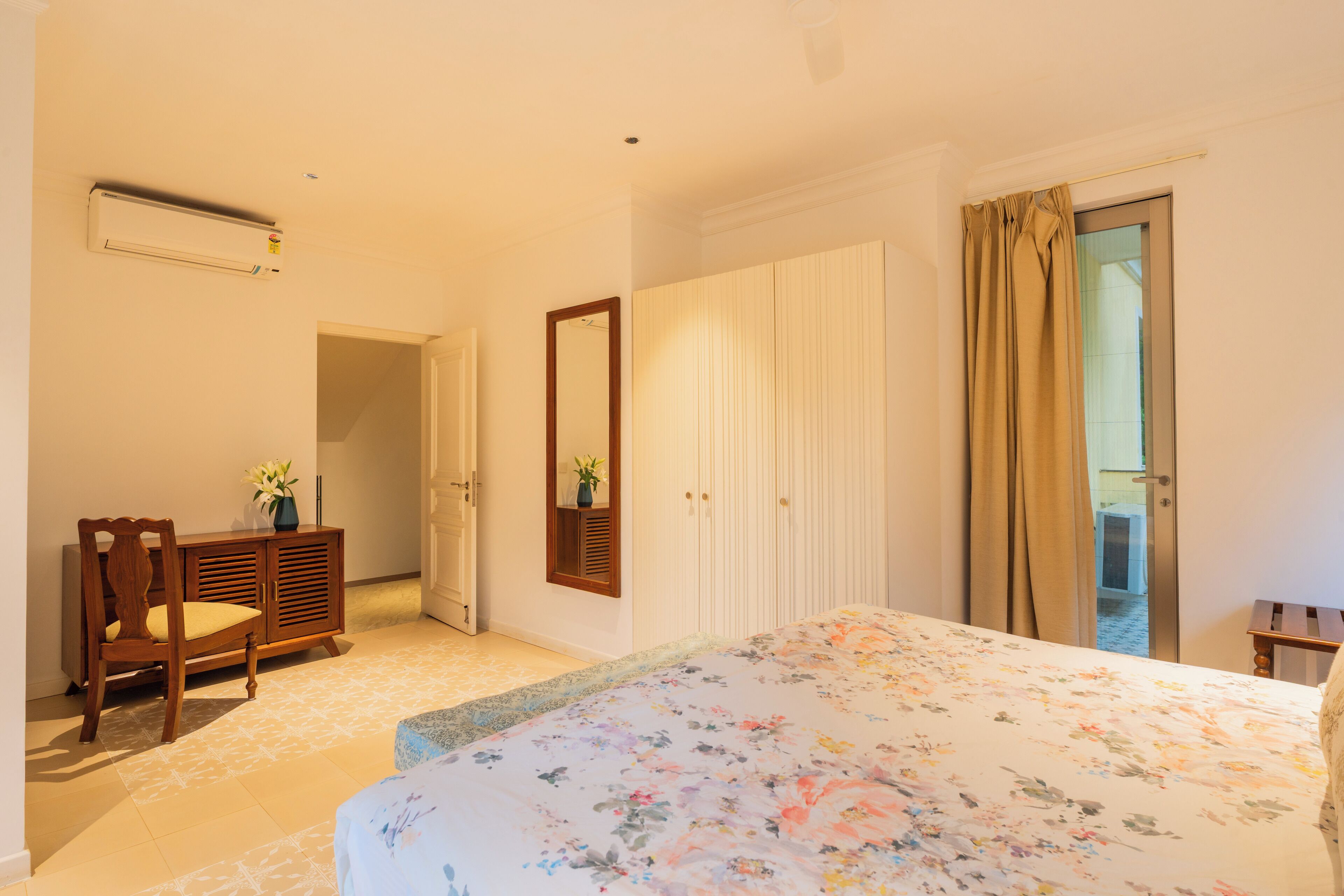 Quarto com cama, penteadeira, espelho e porta que dá para uma varanda.