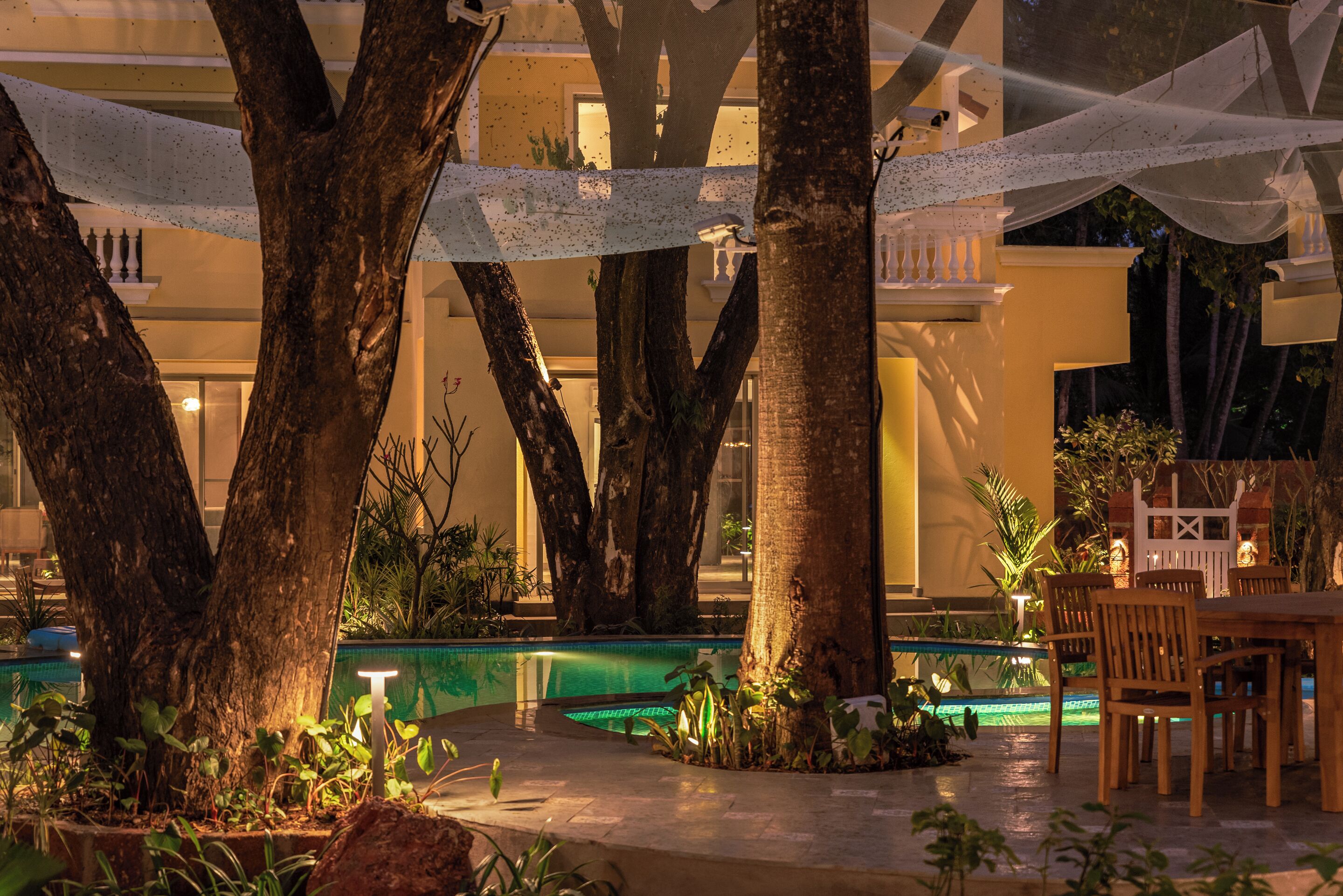 Un área de piscina con árboles, una mesa y sillas.