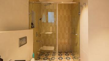 A modern bathroom with a glass-enclosed shower, patterned floor tiles, and a visible toilet.