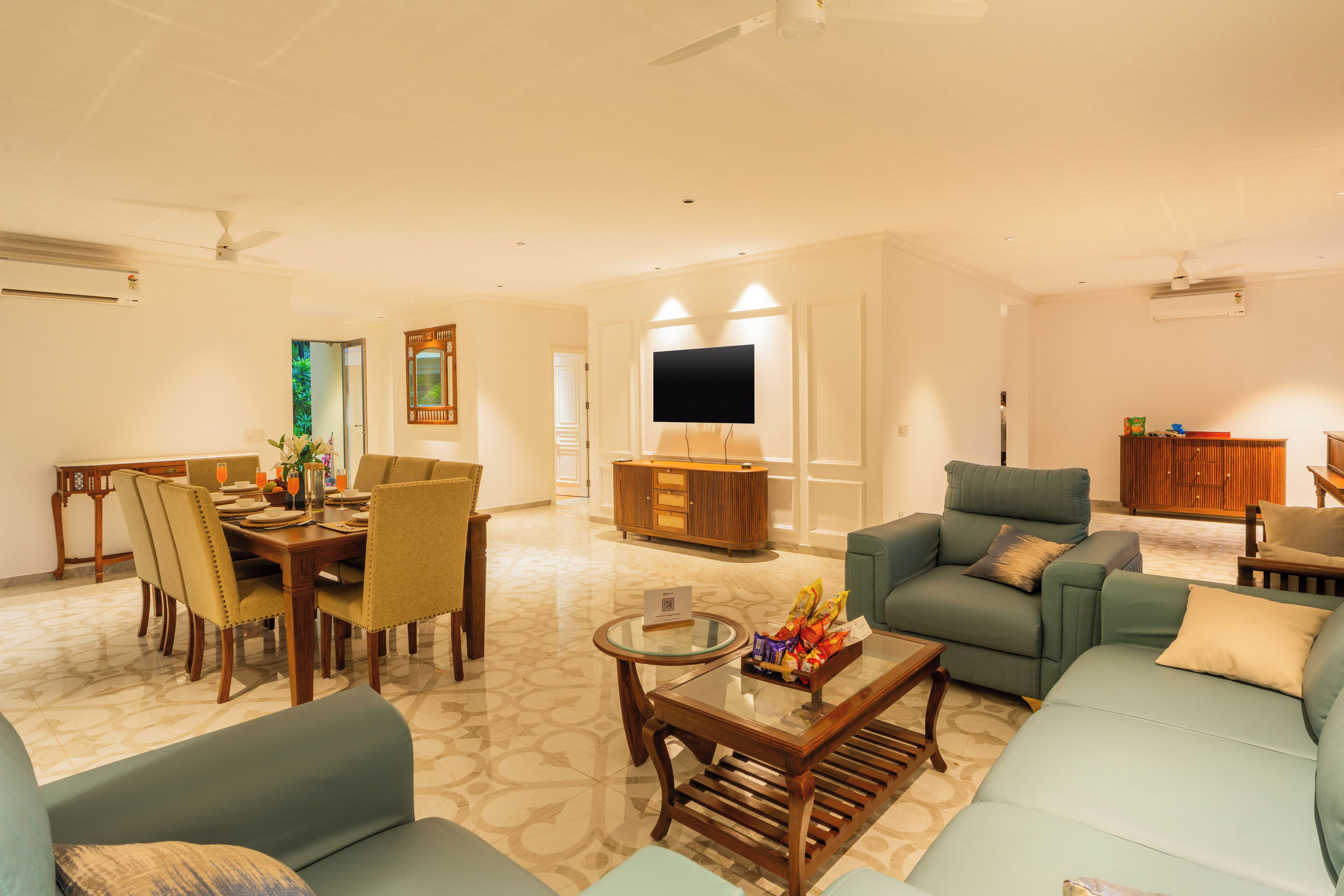 A spacious living room with a dining area, a flat-screen TV mounted on the wall, and a comfortable seating arrangement.