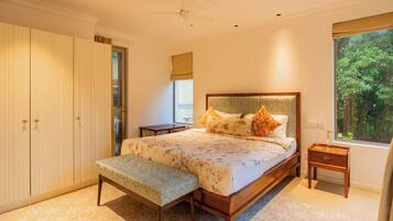A bedroom with a bed, bench, wardrobe, bedside table, and a window with a view of greenery.