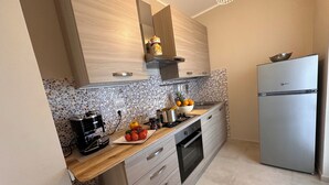 A modern kitchen with wooden cabinets, a stainless steel refrigerator, and a tiled backsplash. - Casa vacanze La Perla. Alghero, Lido Mari Pia area (Alghero)