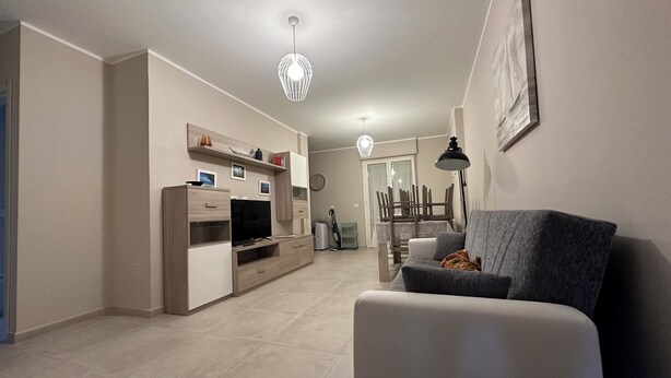 A modern living room with a grey sofa, a TV, and a dining area with a table and chairs. - Casa vacanze La Perla. Alghero, Lido Mari Pia area (Alghero)