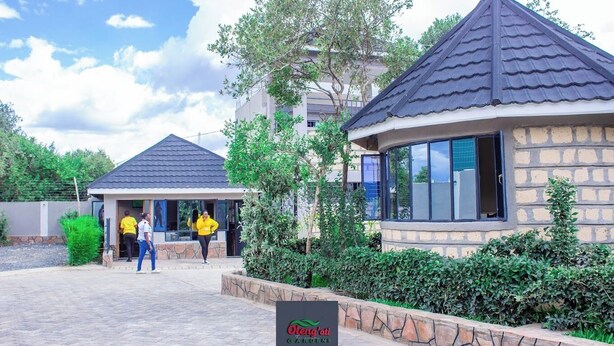 A building with a stone facade and a dark roof, surrounded by greenery and a paved area. - Oleng'oti Gardens Narok (Narok)